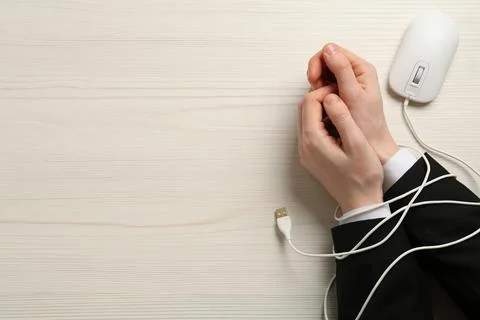 Man showing hands tied with computer mouse cable at white wooden table, top v Stock Photos