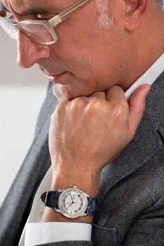 Man showing his watch while thinking with hand on chin looking down Stock Photos