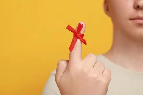 Man showing index finger with red tied bow as reminder against orange backg.. Stock Photos