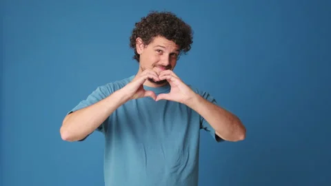 Man showing representing heart in the shape of fingers gesture isolated on blue Stock Footage 252502308