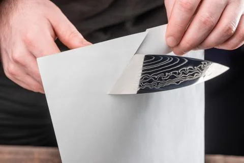 Man showing sharpness of a knife by cutting a thin paper sheet Stock Photos