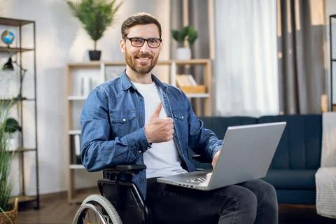 Man showing thumb up while sitting in wheelchair with laptop Stock Photos