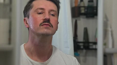 A man is shown performing grooming tasks in front of a bathroom mirror. He Stock Footage 337111619