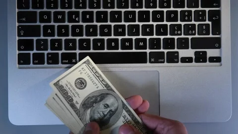 Man shows 1000 dollars in 100 dollar bills on a laptop keyboard computer Stock Footage 148397010