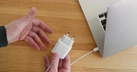 Man shows cord with plug connected to laptop on table Stockbeeldmateriaal 234537856
