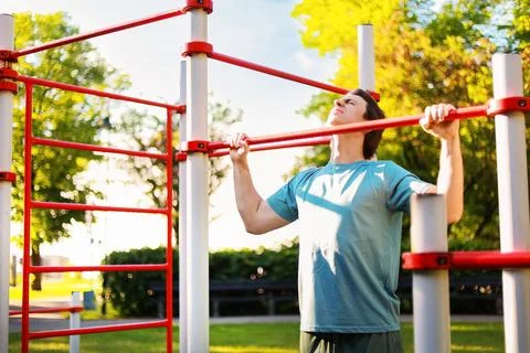 Man shows effort doing a pullup workout outdoors. He builds strength during.. Stock Photos