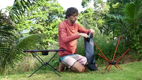 A man shows the process of  disassembling a ultralight travel chair in nature Stock Footage 293693675