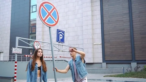 Man shows tricks posing with a lady dressed in casual style before a street sign Stock Footage 80957796