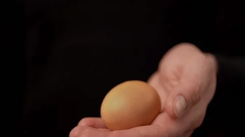 A man shows a yellow egg in front of the camera on a black background. Stock Footage 159366786