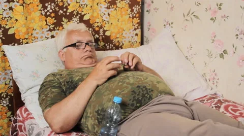 The man is sick in bed and eating pills after wash down with water Stock Footage 64779211