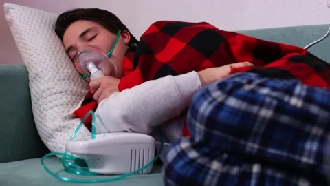 Man is sick in bed at home in front of the TV, breathing with a nebulizer Vidéo 262852989