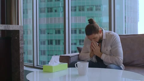 A man is sick, sitting on the couch at home and blowing his nose into a napkin Vidéo 267417422