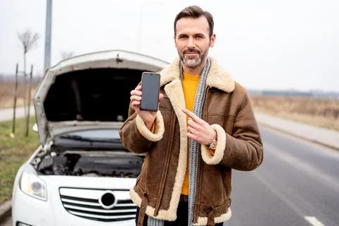 A man by the side of the road is standing in front of a broken car, pointing Foto stock