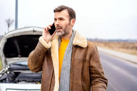 A man by the side of the road is standing in front of a broken car, calling t Stock-Fotos