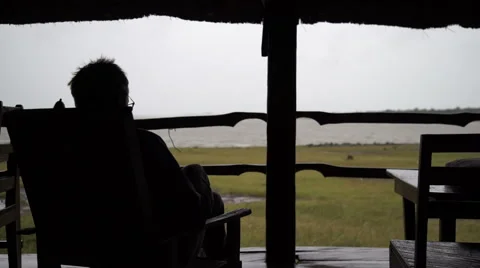 A man in silhouette from the back watching the rain from a hut in Mali, Africa. Stock Footage 67404221