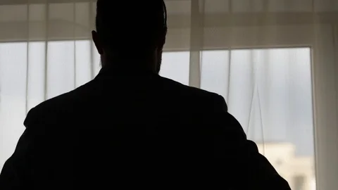 Man in silhouette dressing with a jacket in front of a window for a weading Stock Footage 93079234