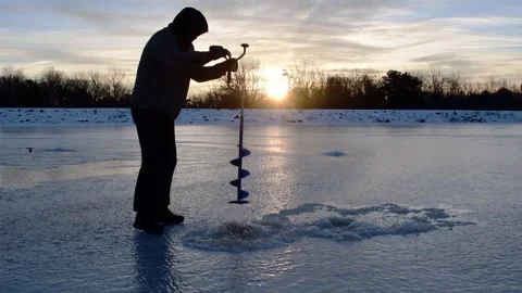 Man in silhouette driling hole in ice, sunrise Stock Footage 255294769