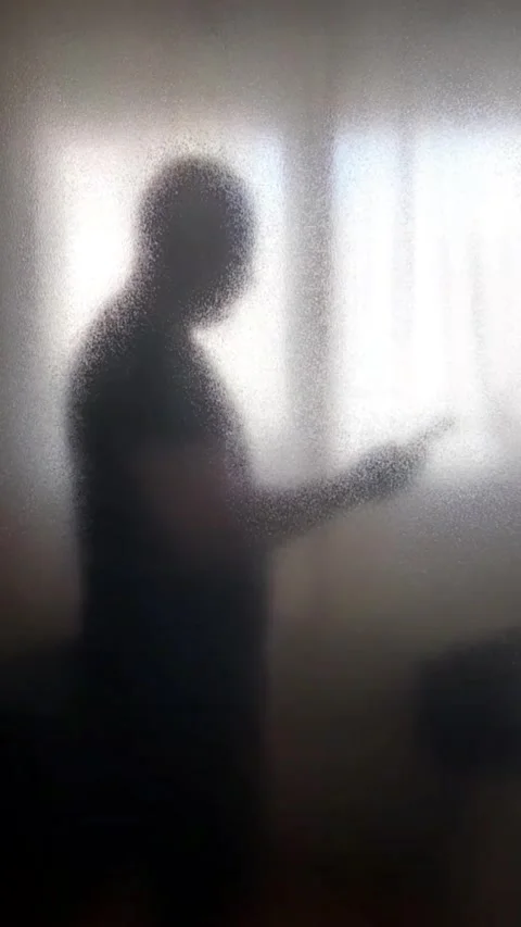 A man in silhouette in front of a window with his hands holding a cell phone, ad Vídeos de archivo 307430671
