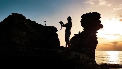 Man silhouette with photo camera in his hands and tripod on the stone. Stock Photos