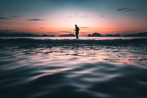 Man silhouette in the sea at sunset with red and blue sky looking at the horizon Stock Photos