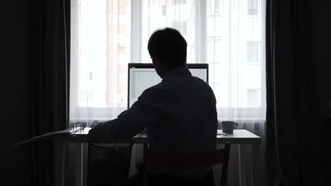 Man in silhouette sitting at a desk with a computer, feeling stressed and Stock Footage 346251085