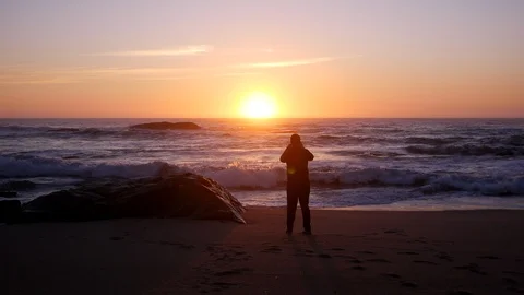 Man in silhouette at sunset on beach, taking photo with cellphone Stock Footage 104681639