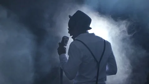 Man singer the view from the back in the smoke and white light sings into a Stock Footage 79340878