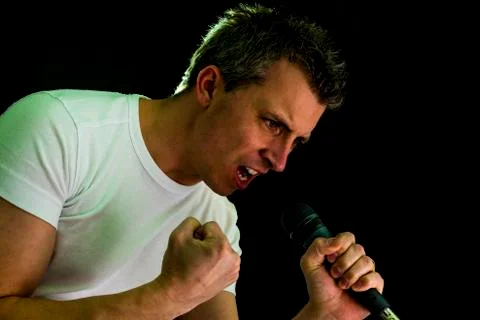 A man singing in a microphone on black background. Photos