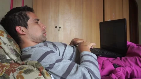 A man singing a song lying on his bed looking at his laptop and typing on it Stockbeeldmateriaal 154812281