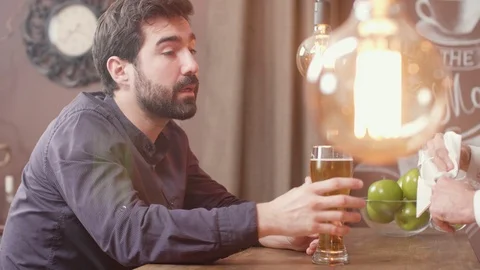 Man sips a bit of beer while at a bar counter talking to the bartender Stock Footage 106705285