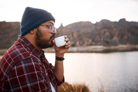 A man sips coffee from a flask while looking at the lake scenery on hiking trip Stock Photos