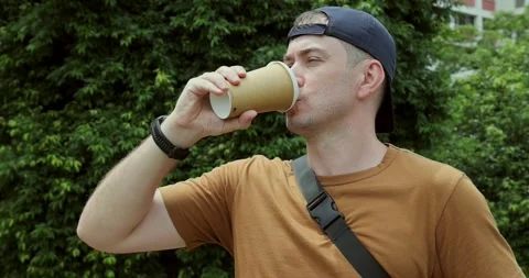 Man Sips Coffee from Paper Cup Outdoors Stock-Footage 323828624