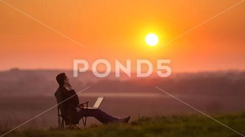 Man sit and work on the laptop by sunset (sunrise) on the top of the hill Stock Photos