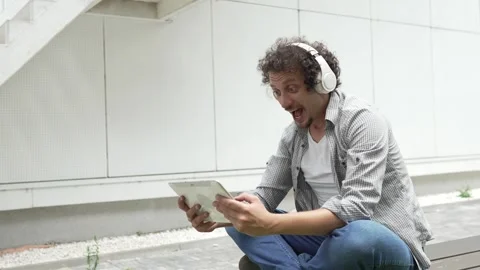 Man sit in front of building use digital tablet to watch movie podcast Stock Footage 248085899