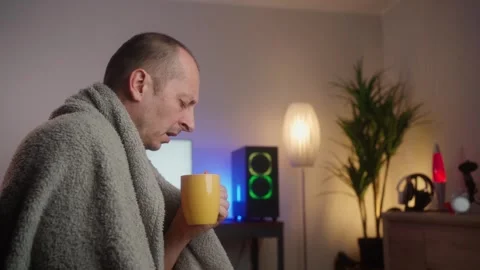 Man sit on sofa bed at home hold cup of tea common cold sneezing, coughing Stock-Footage 269990473