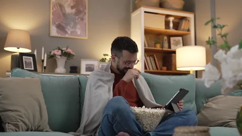 Man sit on the sofa bed watch movie video online use digital tablet Stock Footage 263578340