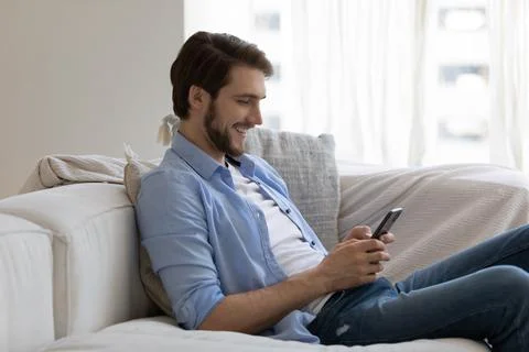 Man sit on sofa holding smartphone share messages through messenger Stock Photos