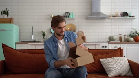 Man sit on sofa open delivered parcel sincerely glad on-line shop Stock Footage 142575519