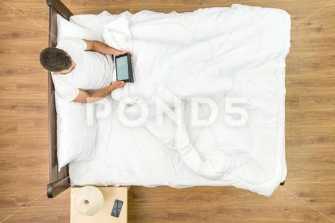 The man sit with a tablet on the bed. View from above Stock Photos