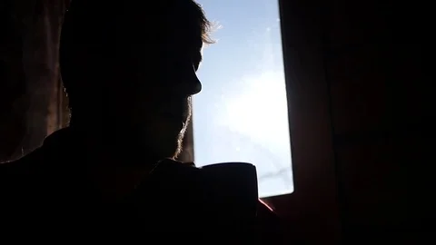 Man sits alone against the window with blue sky, drinking hot tea from a cup Stock Footage 73008443