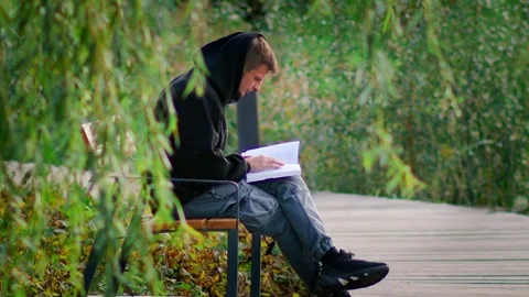 A man sits alone on a park bench, reading a book peacefully Stock Footage 287754675