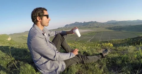 A man sits and drinks coffee on the background of mountains and vineyards Video stock 76474253