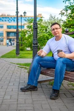 A man sits and eats a bun, in the park on a bench Stock Photos
