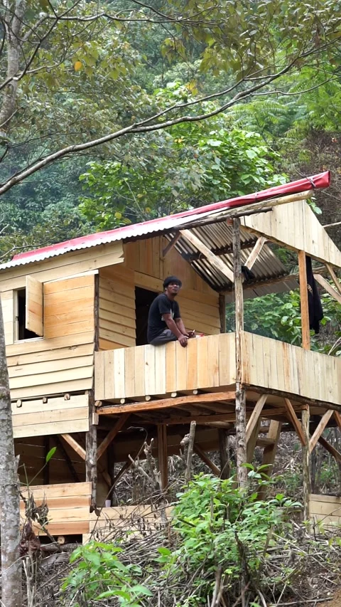 A man sits on the balcony of a newly constructed stilt wooden cabin in the Garut Stock Footage 344093696