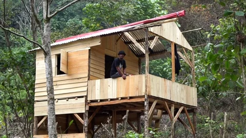 A man sits on the balcony of a newly constructed stilt wooden cabin in the Garut Stock Footage 344093712