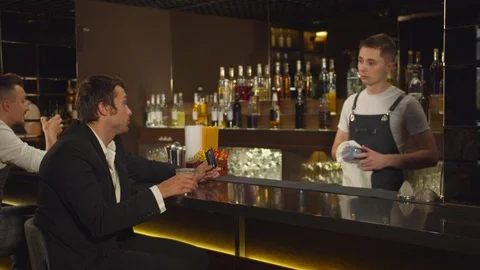 Man sits at the bar, talks to bartender and smiles to someone Stock Footage 123678482