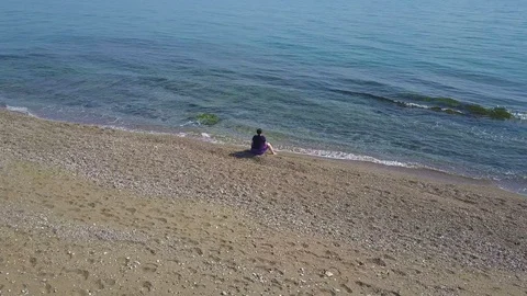 A man sits on the beach, on the beach. The drone flies around. Video stock 93807559