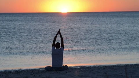 Man sits on the beach next to surf, practicing yoga during amazing sunset Video stock 97152454