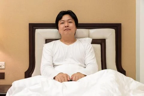 Man sits on bed with calm posture and neutral expression, combining relaxed.. Foto stock