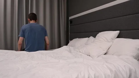 A man sits on the bed falls on his back puts his hands on his head gets up and Stock Footage 307666545